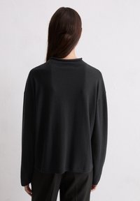 Schwarzer Strickpullover mit lockerem Schnitt, überschnittenen Schultern und hohem Kragen. Glatte Textur, lange Ärmel und schlichtes Design.