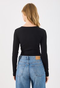 Top preto canelado de mangas longas combinado com jeans denim de cintura alta em azul claro, apresentando um patch de couro liso na cintura.