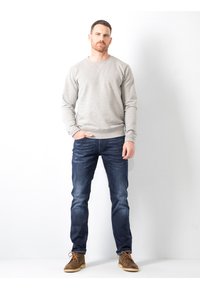Suéter gris claro, jeans azul oscuro y zapatos marrones. El suéter tiene un cuello redondo y puños acanalados. Los jeans son ajustados.