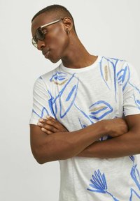 Vit t-shirt med blå och beige abstrakta mönster, rund halsringning, korta ärmar och en mjuk textur.