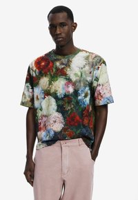 Kurzärmliges Floral-T-Shirt mit lebendigen Farben, das eine Mischung aus roten, weißen und blauen Blumen vor einem dunkelgrünen Hintergrund zeigt.