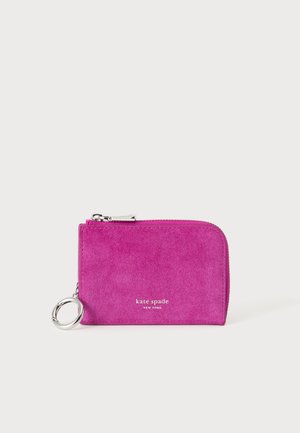 Jasnoróżowy zamszowy portfel na suwak ze srebrnym zamkiem i brelokiem do kluczy, logo "kate spade NEW YORK" w białym kolorze z przodu.