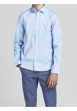 Chemise bleu clair à manches longues avec un col pointu et une texture lisse. Portée avec un pantalon bleu, affichant un look soigné.