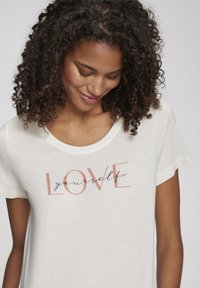Weißes Baumwoll-T-Shirt mit dem Aufdruck "LOVE yourself" in einer Mischung aus Roségold und Marineblau, mit lockerer Passform und Rundhalsausschnitt.