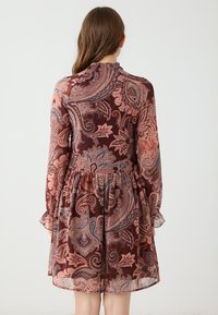 Kurzes, braunes Paisleymuster-Kleid mit langen, durchsichtigen Ärmeln und einem rüschierten Saum. Es hat kunstvolle Muster in Blau-, Creme- und Rosttönen.