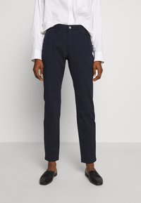 Tummansiniset chinot, joissa on kapea malli, etutaskut, nappikiinnitys ja sileä puuvillakangas. Yhdistetty mustiin liukuviin kenkiin.