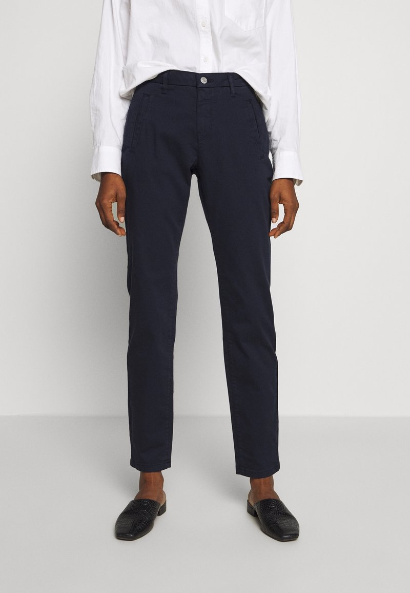 Tummansiniset chinot, joissa on kapea malli, etutaskut, nappikiinnitys ja sileä puuvillakangas. Yhdistetty mustiin liukuviin kenkiin.