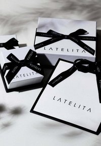 Three white gift boxes with black logo "LATELITA," featuring black satin ribbons. The largest box has a geometric shape and black edges.