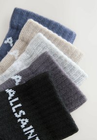 Zloženi kup petih zloženih pletenih nogavic v črni, temno sivi, svetlo sivi, bež in modri barvi, vsaka z delno vidnim belim napisom na manšeti.