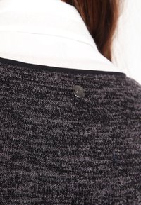 Svart och grå texturerad stickad tröja med rundad halsringning, prydd med en dekorativ svart knapp bak och ett kontrasterande vitt innerlager.