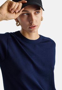 Granatowy sweter dzianinowy z okrągłym dekoltem, przedstawiony z gładką teksturą, z subtelnymi szwami na ramionach i dopasowanymi rękawami.