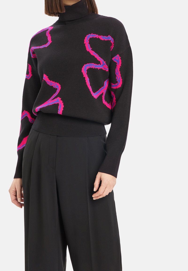 Svart polotröja med djärva rosa och lila abstrakta mönster, tillsammans med högmidjade vida svarta byxor.