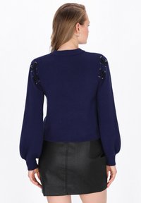Pulover tricotat de culoare bleu marin, cu mâneci bufante, având detalii cu dantelă cusută pe umeri. Asortat cu o fustă mini din piele neagră.