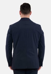Blazer blu navy con una texture liscia, vestibilità su misura e spacco singolo sul retro. Presenta spalle strutturate e polsini con bottone.