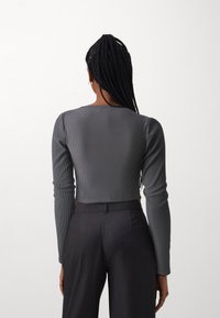 Grauer gerippter Langarm-Crop-Top mit Rundhalsausschnitt, kombiniert mit hochgeschnittenen dunklen Hosen, die eine glatte Textur und eine taillierte Passform aufweisen.