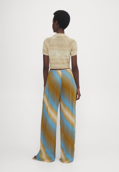 Beige gebreide polo met korte mouwen, gecombineerd met wijde broekspijpen met diagonale strepen in blauw, bruin en crème. Soepele textuur.