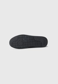 Semelle en caoutchouc noir avec des motifs de texture antidérapants et le logo Lacoste sur un fond clair.