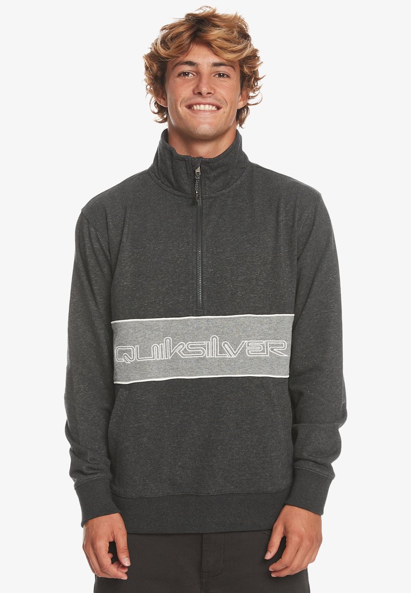 Pullover in pile grigio con colletto alto, zip a quarto e una fascia grigia a contrasto con il logo "Quiksilver" in bianco. Texture morbida e vestibilità comoda.