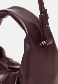 Borsa a tracolla in pelle burgundy con design piegato, texture liscia e un dettaglio in metallo argento sul manico regolabile.