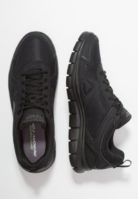 Black athletic shoes with mesh fabric upper, cushioned sole, and rubber tread. Features include laces and a pull tab on the heel.
