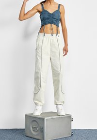 Ljust blå rynkad croppad topp med justerbara snören, i kombination med krämfärgade cargobyxor med elastisk midja som har grå piping och dragkedjor. Vita sneakers.