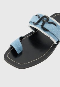 Blue denim slide sandal with a black rubber sole, featuring a frayed strap and a decorative black metal accent.