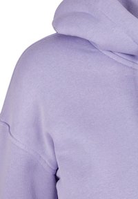 Gros plan sur un sweat à capuche lavande doux montrant le tissu texturé et les détails des coutures d'épaule.