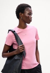 Lyserød bomulds t-shirt med korte ærmer og rund halsudskæring, forsynet med et logo i midten, parret med en sort læder tote-bag.