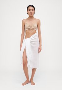 Beige stripete bikinitopp med frontknute, kombinert med et langt hvitt omslagsskjørt med duskdetaljer og en sideslitt.