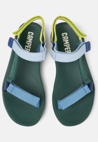 Grüne Sandalen mit verstellbaren blauen und gelben Riemen, einem strukturierten Fußbett und einer konturierten Form für Komfort. Sichtbares Branding.