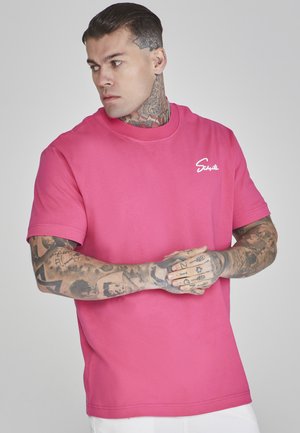 Camiseta de algodón de manga corta en color rosa, con cuello redondo y un logo blanco en el lado izquierdo del pecho. Textura suave y ajuste relajado.
