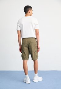 Camiseta blanca de manga corta combinada con pantalones cortos cargo en color verde oliva que presentan bolsillos laterales y un ajuste holgado. El modelo lleva zapatillas blancas.