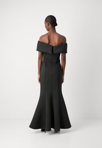 Robe noire décolletée, avec un corsage ajusté, un nœud structuré au niveau du col, une jupe évasée et une texture lisse.