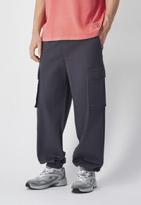 Marine cargobroek met elastische boorden, voorzien van meerdere zijzakken en een losse pasvorm. Gecombineerd met grijze sportschoenen.