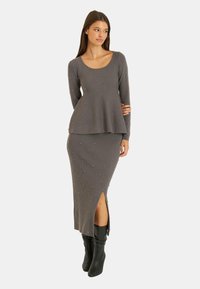 Robe grise à côtes avec des manches longues, taille peplum évasée et strass décoratifs. Elle présente une fente sur le côté et est associée à des bottes noires jusqu'aux genoux.