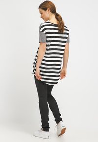 Túnica listrada em preto e branco com mangas curtas listradas, leggings pretas e ténis brancos. A túnica tem uma parte de trás mais longa e um corte descontraído.