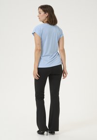 Haut bleu clair à manches courtes avec une coupe décontractée, associé à un pantalon noir évasé. Texture lisse, design simple, et vue arrière mise en avant.
