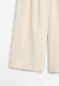 Close-up of beige lightweight fabric pants with wide legs and visible stitching near the hem.