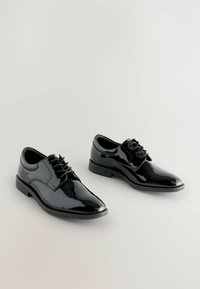 Chaussures habillées en cuir verni noir avec un bout pointu, un laçage et des côtés texturés. Semelle en caoutchouc plate, mettant en valeur un style moderne et épuré.