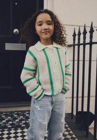 Crochet cardigan in cream with green, pink, and purple stripes, featuring a collar and three buttons. Worn with distressed light jeans.