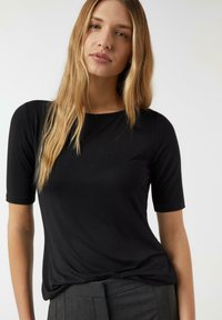 Czarny top z krótkim rękawem wykonany z gładkiej, lekkiej tkaniny. Posiada okrągły dekolt i luźny krój, zestawiony z szarymi, szytymi spodniami.