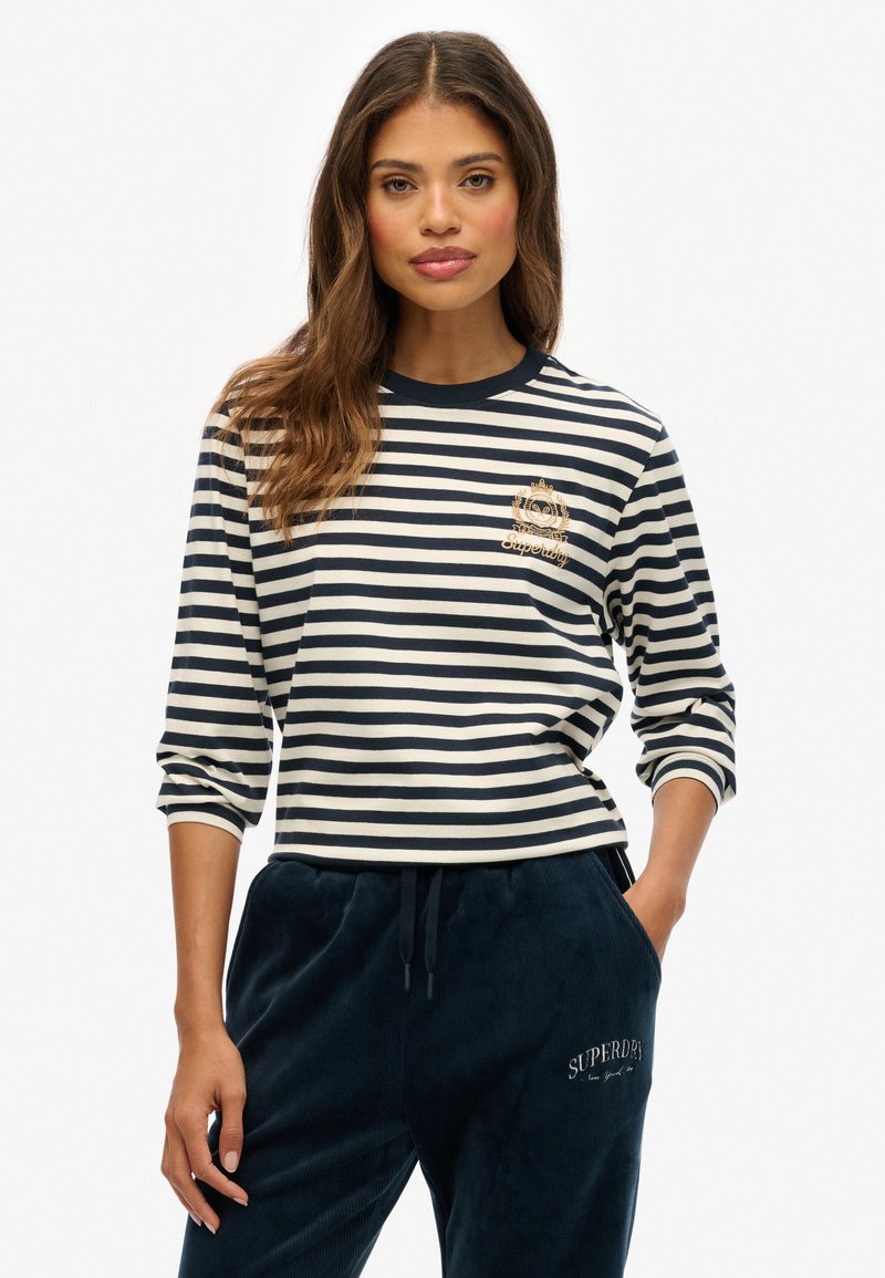 Stribet langærmet skjorte i marineblå og creme med rund hals og logo broderet på brystet, stylet med marineblå fløjl bukser.