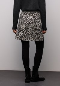 Hame selimut macan tutul dalam warna beige dan hitam, dengan desain lebar, dipakai di atas legging hitam dan dipadukan dengan sepatu boot pergelangan hitam.