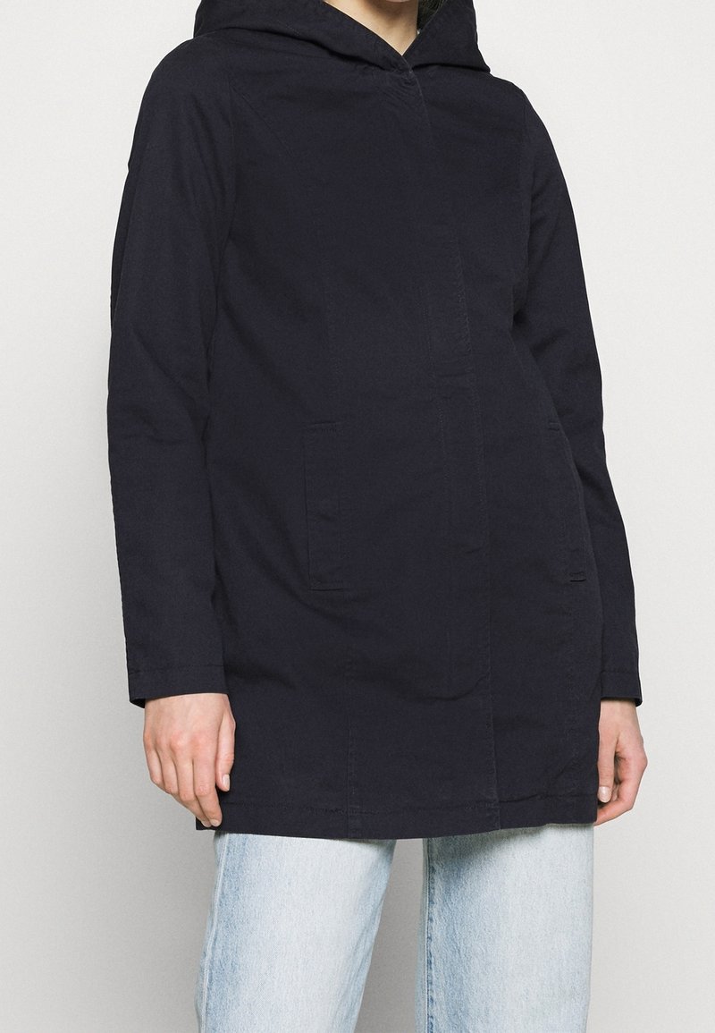 Cappotto con cappuccio di colore blu navy, a taglio dritto, con due tasche frontali e una texture liscia. Chiusura a bottoni coperta e dettagli di cucitura minimi.