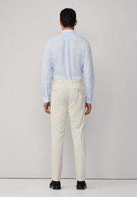 Himmelblaues, langärmliges Hemd mit dezentem Streifenmuster, kombiniert mit cremefarbenen Hosen. Das Outfit hat einen klassischen Kragen und eine taillierte Passform.