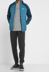 Blå vadderad jacka med huva, grå T-shirt, mörkgrå träningsbyxor och svarta skor med ljusbeigea sulor. Har kontrasterande sömmar.