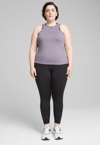 Lila, ujjatlan sportpóló virágmintákkal, fekete leggings-szel, amelynek alján textúrált minta található. Fehér sportcipők.
