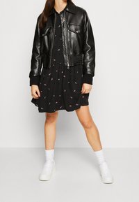 Svart läder bomberjacka med två framlomm pockets och ribbade muddar, matchad med en svart klänning med små rosa mönster och vita sneakers.