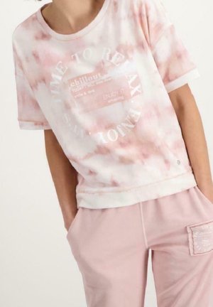 Persona che indossa una maglietta tie-dye rosa e bianca con la scritta "Time to Relax" e pantaloni rosa coordinati con una tasca laterale a toppa.