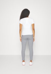 T-shirt bianco aderente abbinato a leggings grigi. I leggings sono elasticizzati con una texture liscia. Sneakers bianche con dettagli rosa completano il look.